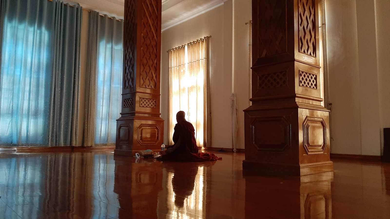 A monk seated in deep meditation in a sunlit hall — a posture of complete stillness