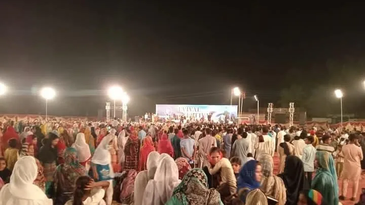 A large outdoor revival gathering at night in Pakistan, the crowd lit by stage lights